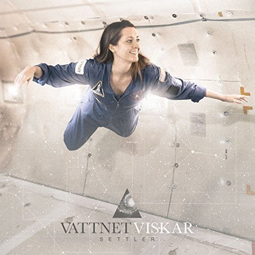 A woman in a blue jumpsuit floats in mid-air against a concrete wall.