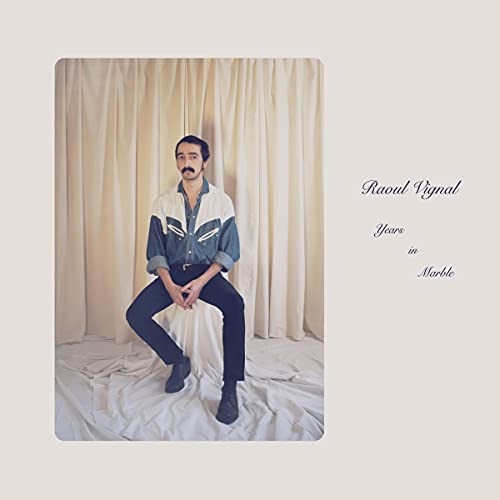 "CD cover featuring a man sitting on a white sheet with beige curtains."
