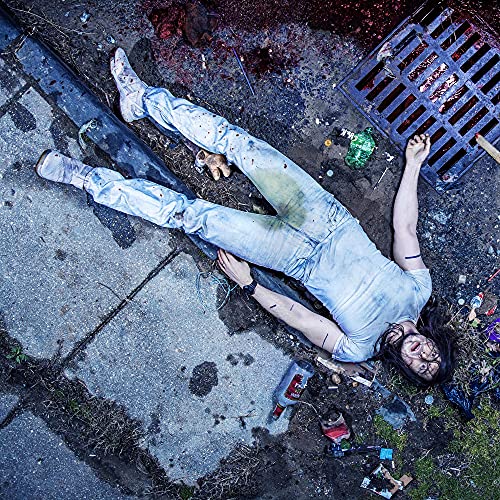 A person lying on the ground next to a storm drain with scattered trash.