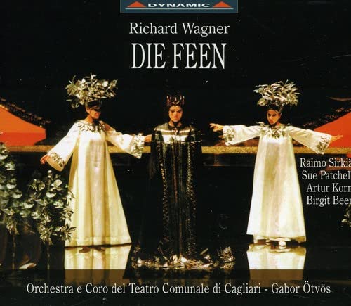 Three performers in elaborate costumes and headpieces stand on a stage for Die Feen.