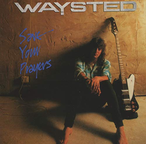 A man with long hair sits on the floor next to a bass guitar.