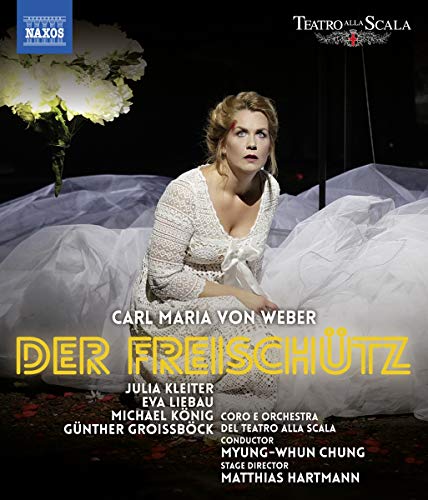 "Blonde woman in white dress kneeling, surrounded by white fabric and flowers."