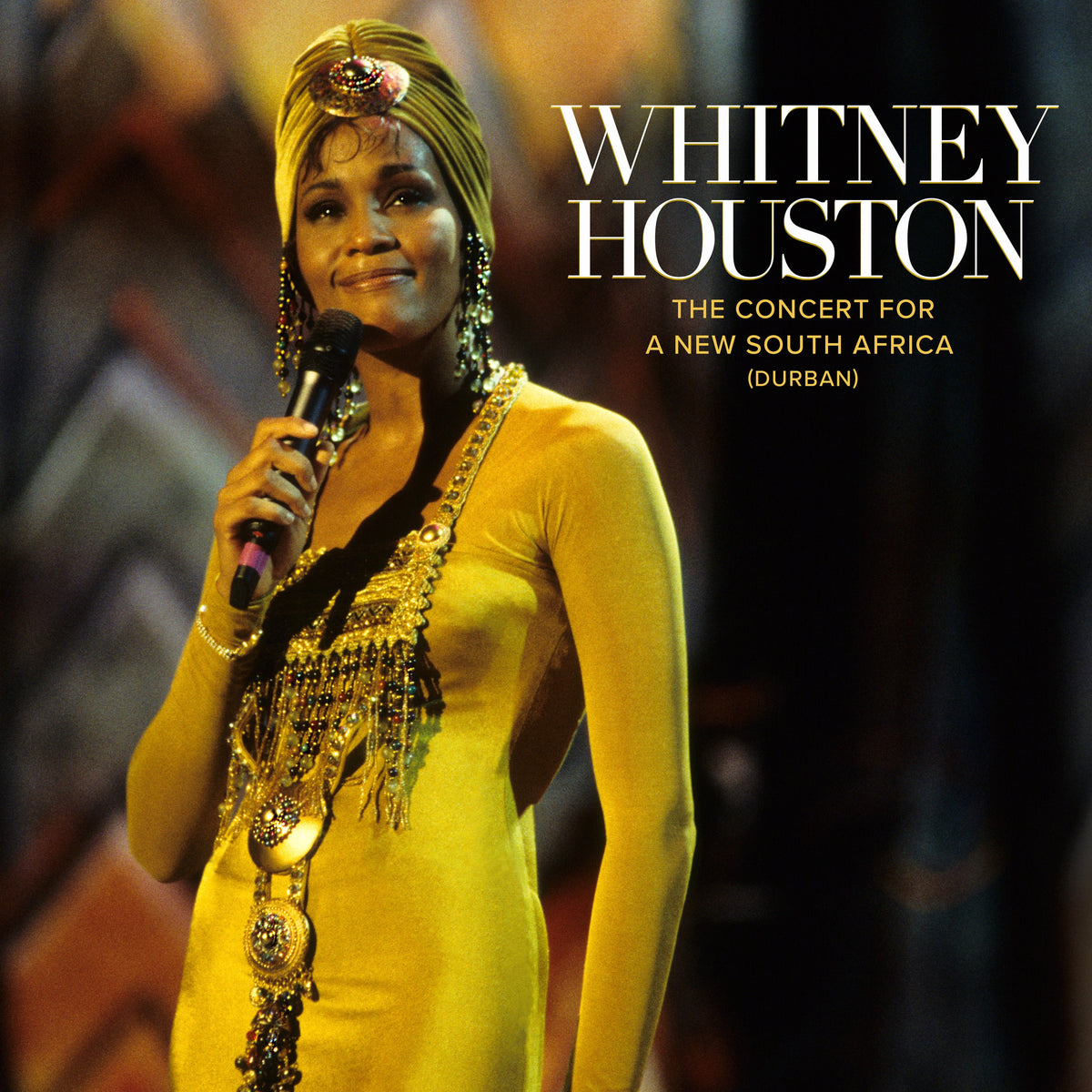 Whitney Houston in yellow gown singing into a microphone onstage.