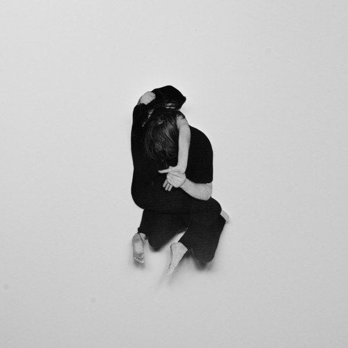 Black and white image of a person crouching, with their head down, against a plain background.