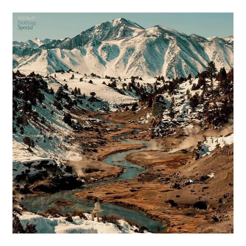 A person stands by a winding stream in a snowy mountain valley landscape.