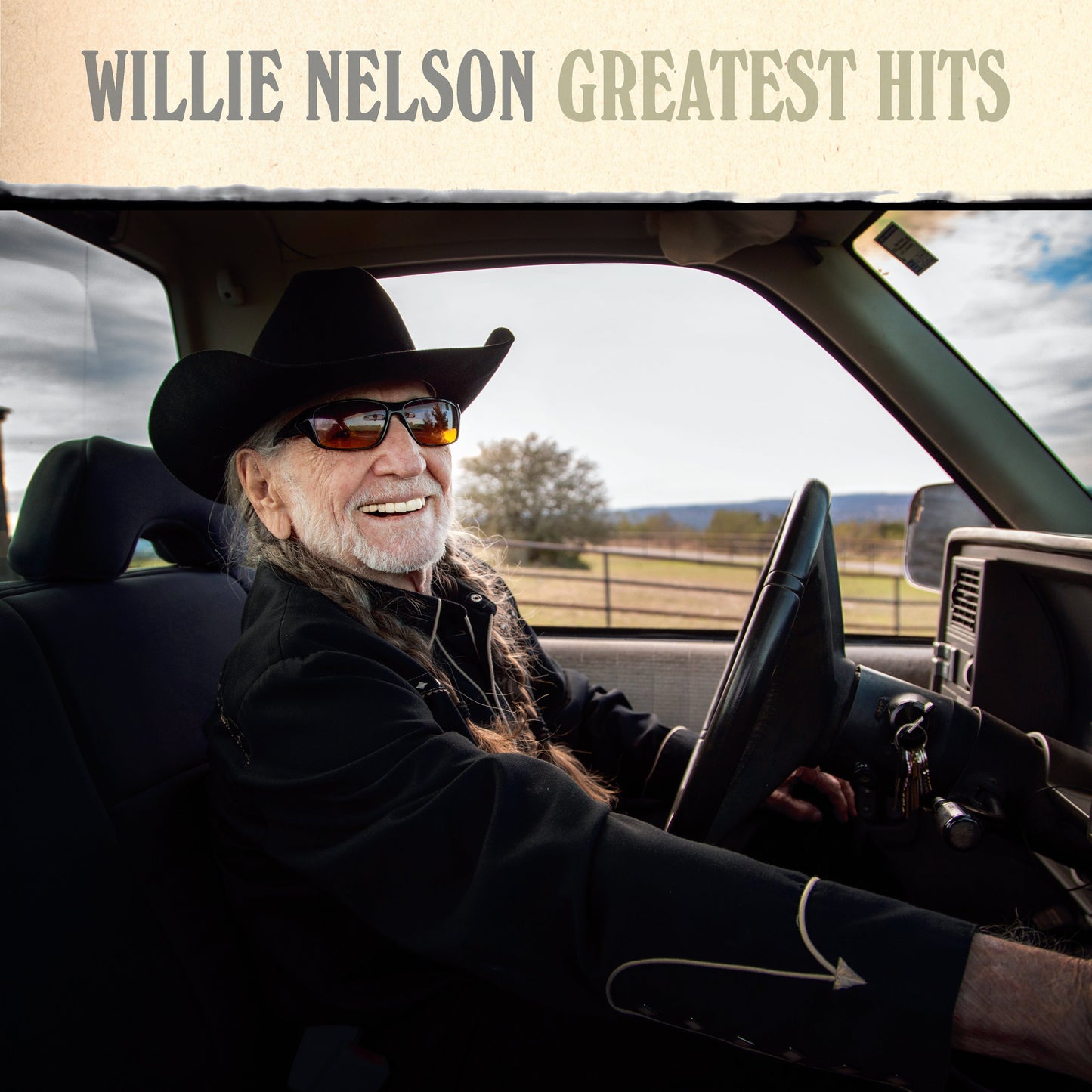 Willie Nelson smiling while driving, album cover for “Greatest Hits.”