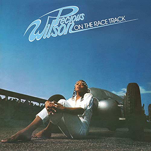 Album cover: woman sitting by a car on a racetrack.