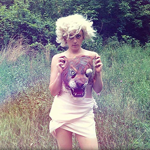 A person in a white dress holds a tiger mask in a grassy field.