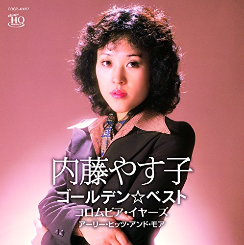 Portrait of Yasuko Naito with curly hair wearing a suit against a pink background.