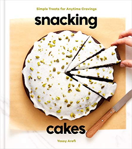 A round cake with white frosting and pistachios on parchment paper, being sliced by hand.