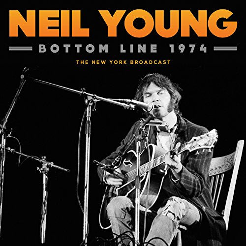 Neil Young playing acoustic guitar on stage, black and white photo.