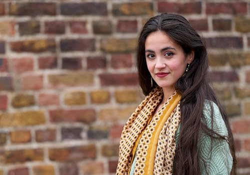 Woman with long dark hair and patterned scarf, brick wall background.