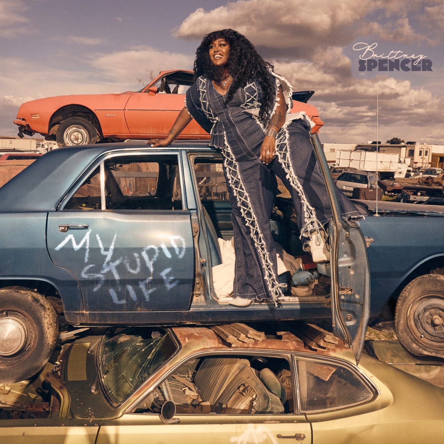 Brittney Spencer album cover featuring a woman standing on wrecked cars.