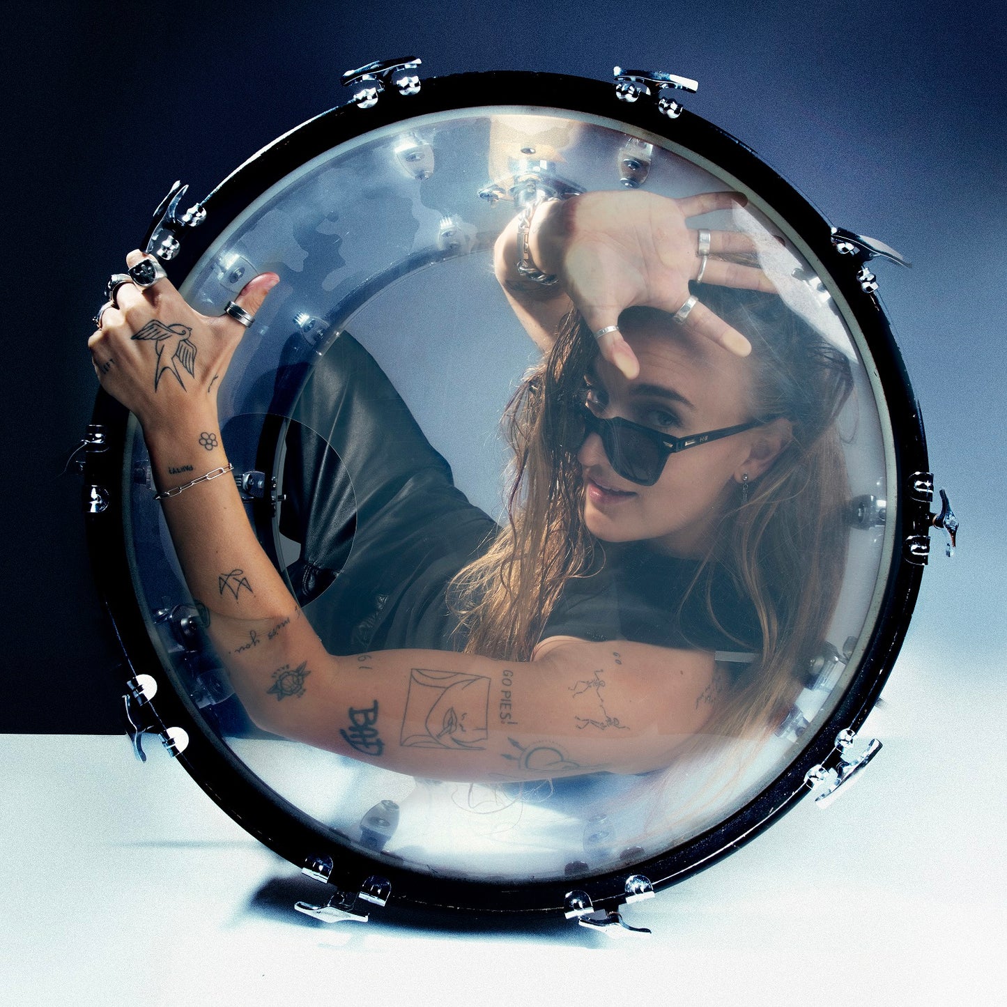 G Flip reflected in a snare drum, wearing sunglasses and tattoos.
