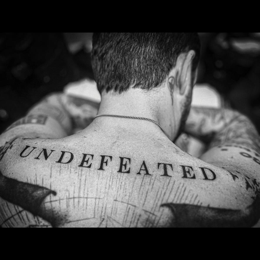 Black and white photo of a man’s back with the word “UNDFEATED” tattooed on it.