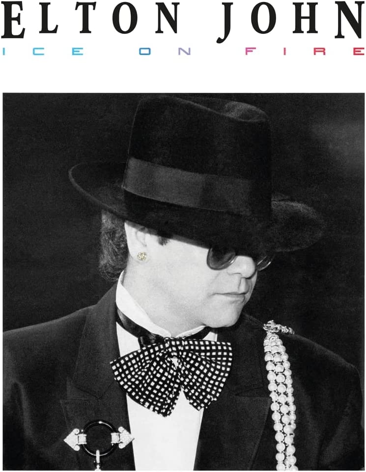 Black and white portrait of Elton John in a hat and bow tie.
