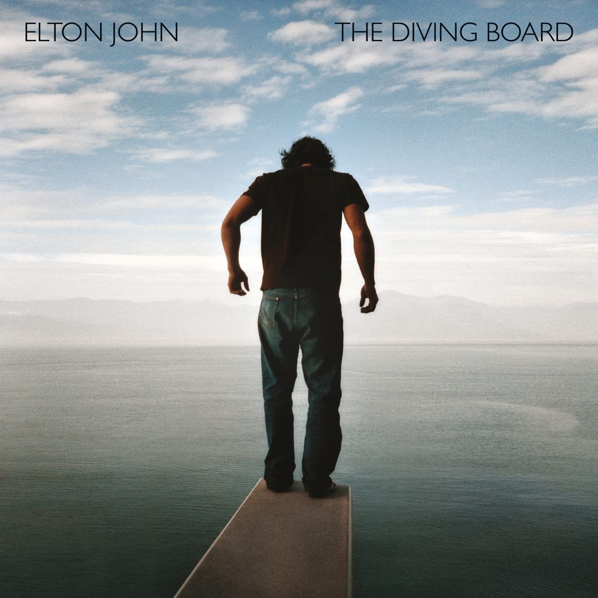 Man standing on a diving board overlooking a blue ocean and sky.