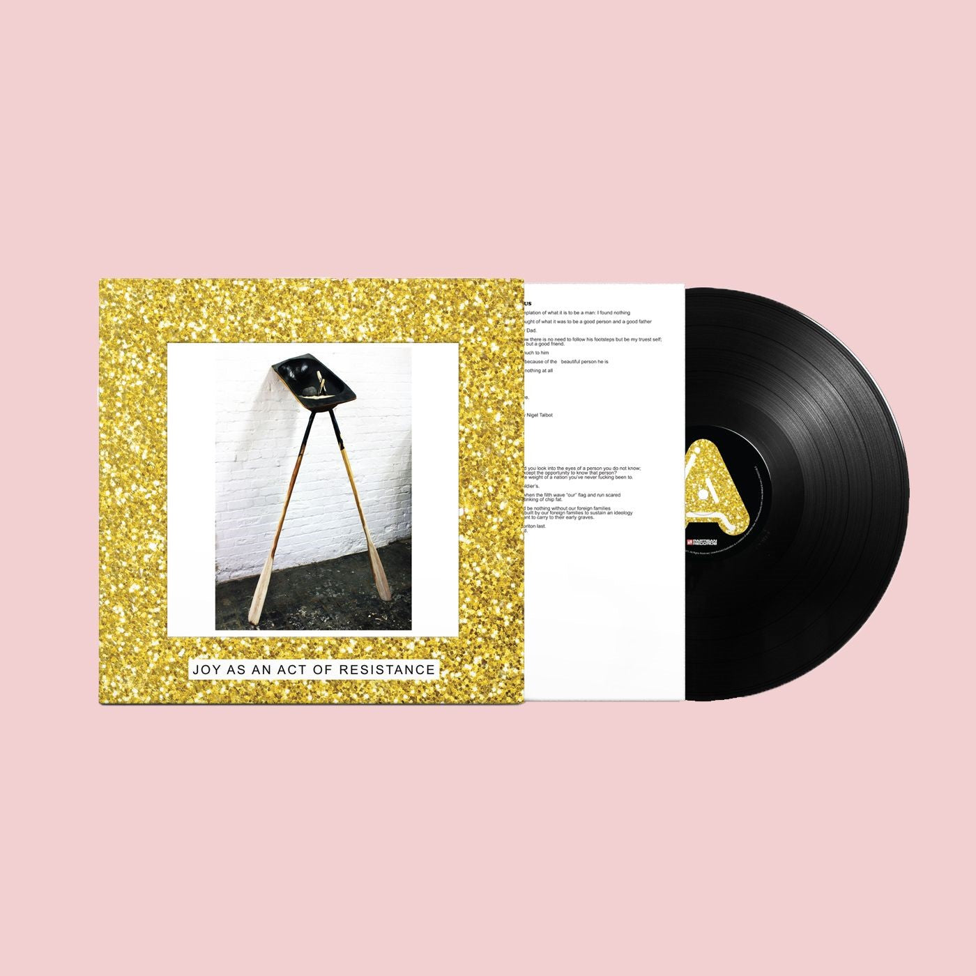 Album cover: a black shovel on a tripod against a white brick wall.