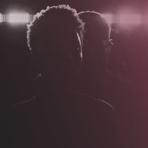 Dark, close-up portrait of two people, likely Denitia & Sene, in shadow.