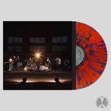 Album cover showing a band performing on stage next to a red-blue splatter vinyl.