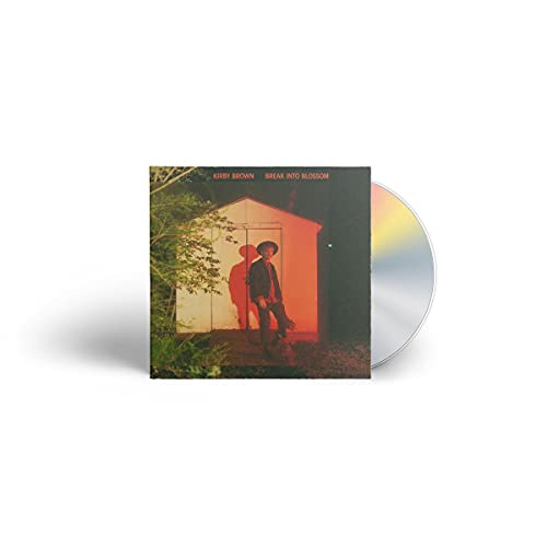 CD cover featuring a person in a suit standing by a small building.
