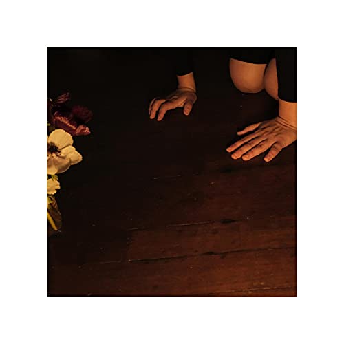 Hands reaching over flowers on a dark wooden surface.