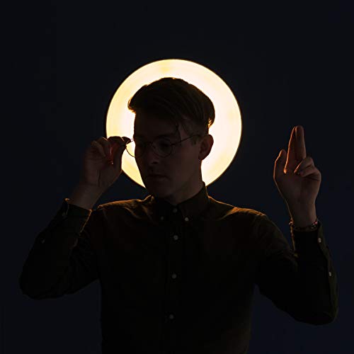 Man with glasses against a bright circular light, dark background.