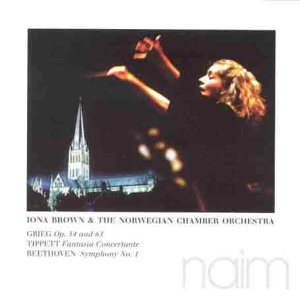 Conductor Iona Brown leads an orchestra, with a church steeple in the background.