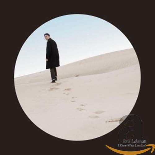 Man in black coat walking on a sandy dune, circular frame.