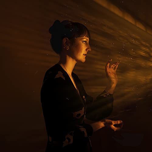 Woman in dark clothing with glowing sparks around her hands.