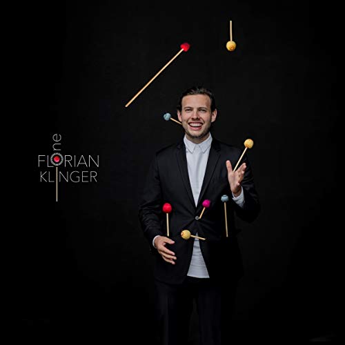 Man in a black suit juggling mallets against a black background with artist name.