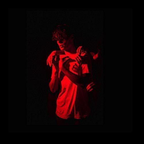 Red-toned portrait of a person embracing themself in darkness.