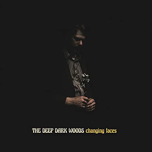 A man holding a guitar, surrounded by darkness, on a black album cover.