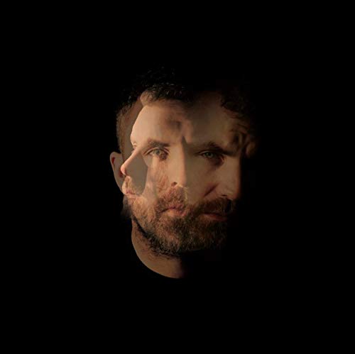 "Man with short dark hair and beard, lit from the side against a black background."