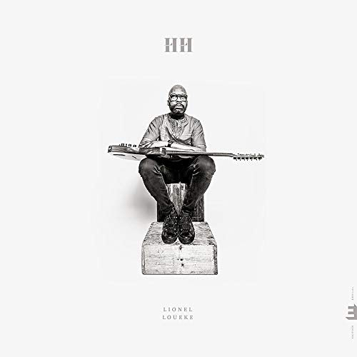 Black and white image of a man sitting on a crate, holding a stringed instrument.