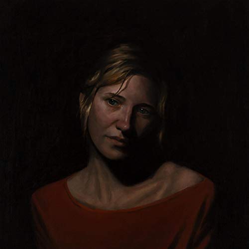 A woman with short blonde hair and a red top is partially shadowed against a black background.