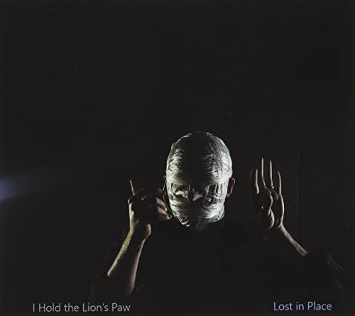 Person with head wrapped in tape, hands raised, dark background.