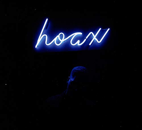 Man's silhouette under blue neon sign reading "hoax" against a dark background.