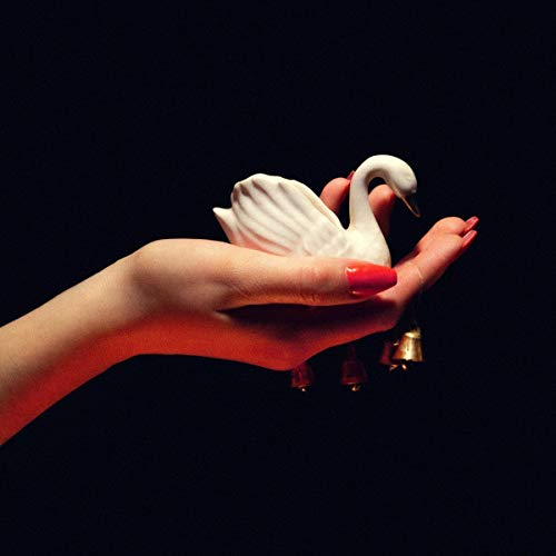 Hand holding a white swan figurine with small golden bells below.