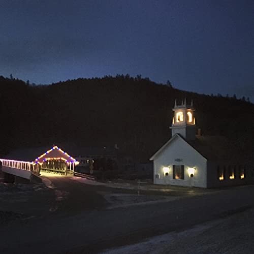 Night scene of a white church and covered bridge with lit windows.