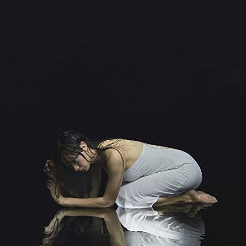 Woman in white dress kneeling, head down, reflected in water.