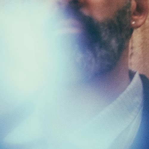 Close-up of a man with a beard, blurred blue and white tones.