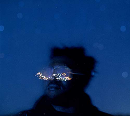 Close-up of a man wearing reflective sunglasses, dark background.
