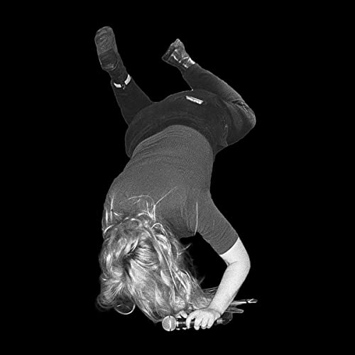 Black and white photo of a person doing a handstand with a microphone.