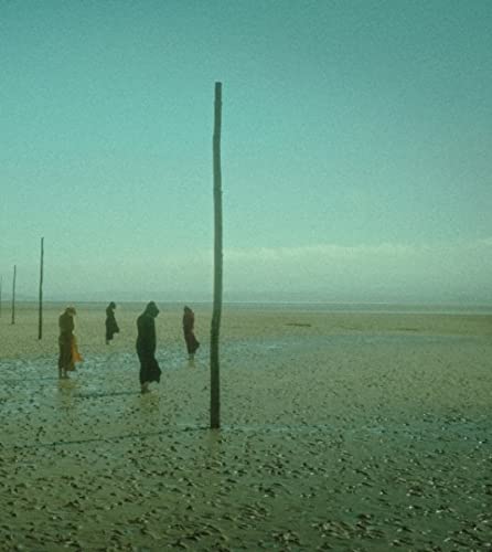 Figures in dark clothing stand in a vast, wet, sandy landscape.