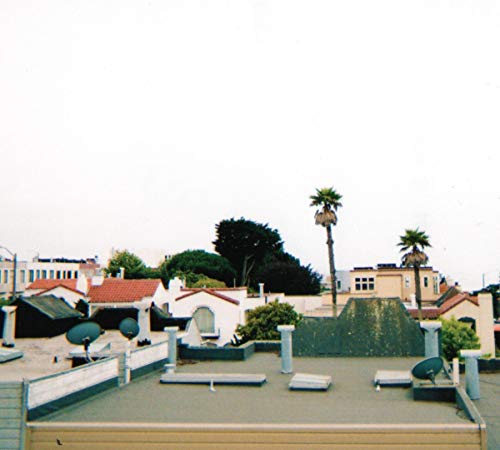 Rooftop view with palm trees, satellite dishes, and buildings under a cloudy sky.