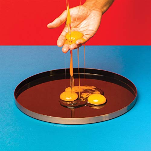 A hand drips yellow liquid onto a mirrored tray against a red and blue background.