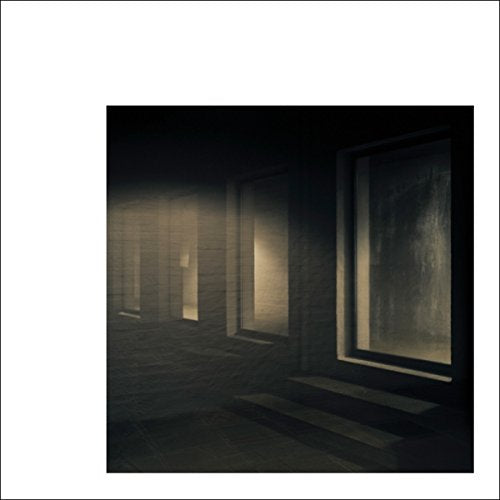 The image depicts a dimly lit, dark-toned album cover with three rectangular cutouts. A concise, descriptive alt text for this image is: "Dark album cover with three rectangular cutouts and a white border."
