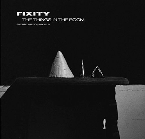 "Black and white album cover with three abstract objects on a table, against a dark background."