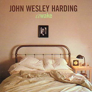 Album cover for "Awake" by John Wesley Harding, featuring a messy bed and nightstand.
